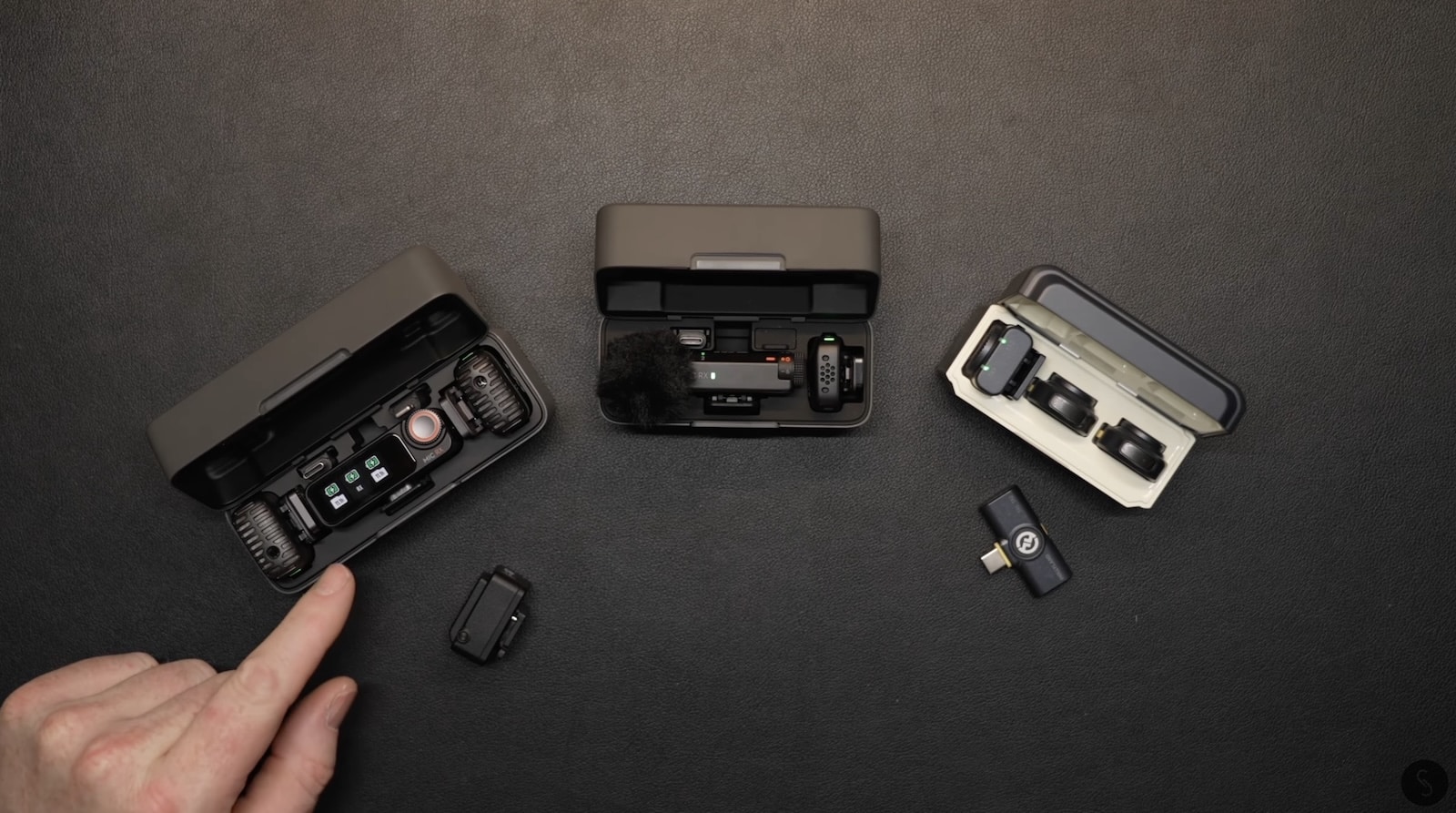 Three wireless microphone kits laid out in their charging cases on a desk.