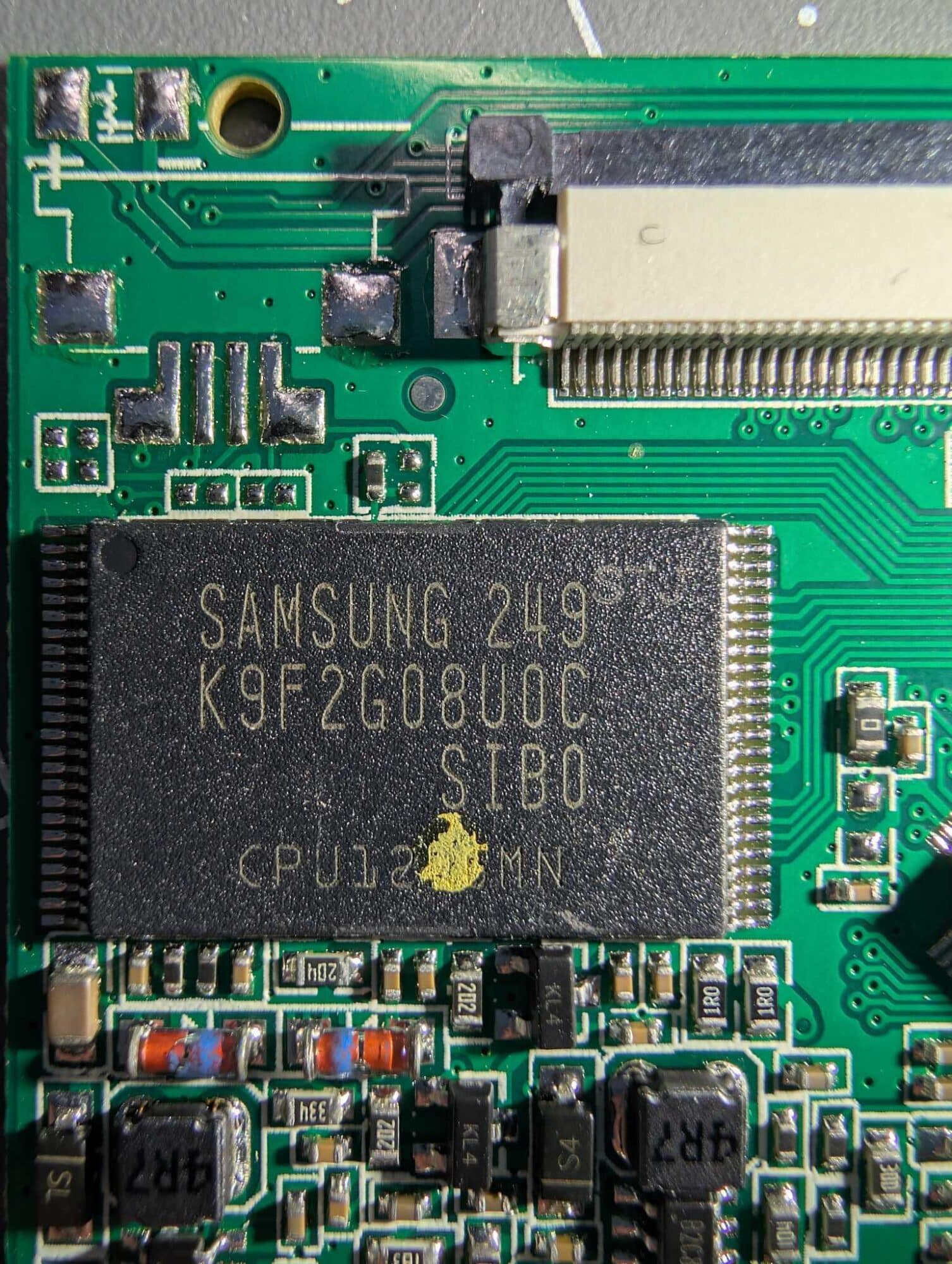 Green circuit board with a Samsung flash memory chip and a ribbon connector.