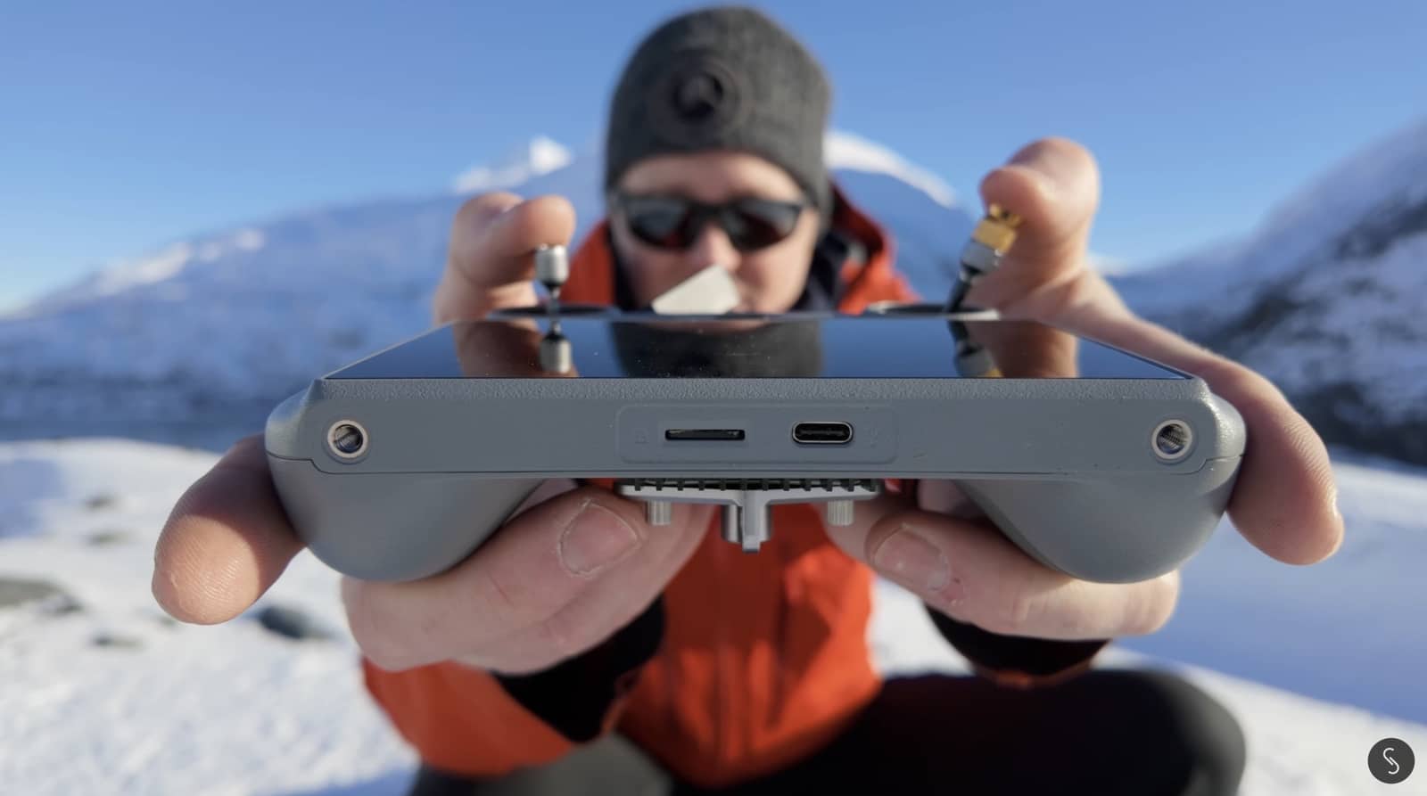 Pilot on a snowy ridge threading control sticks into an upturned DJI RC2.