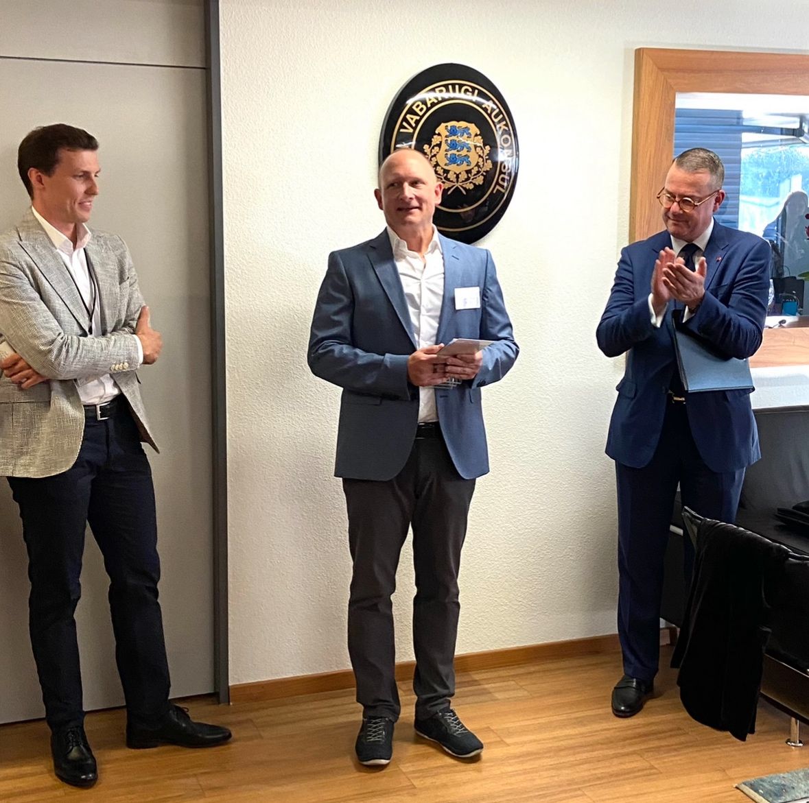 Three men in a small office as one receives an Estonian chamber of commerce award.