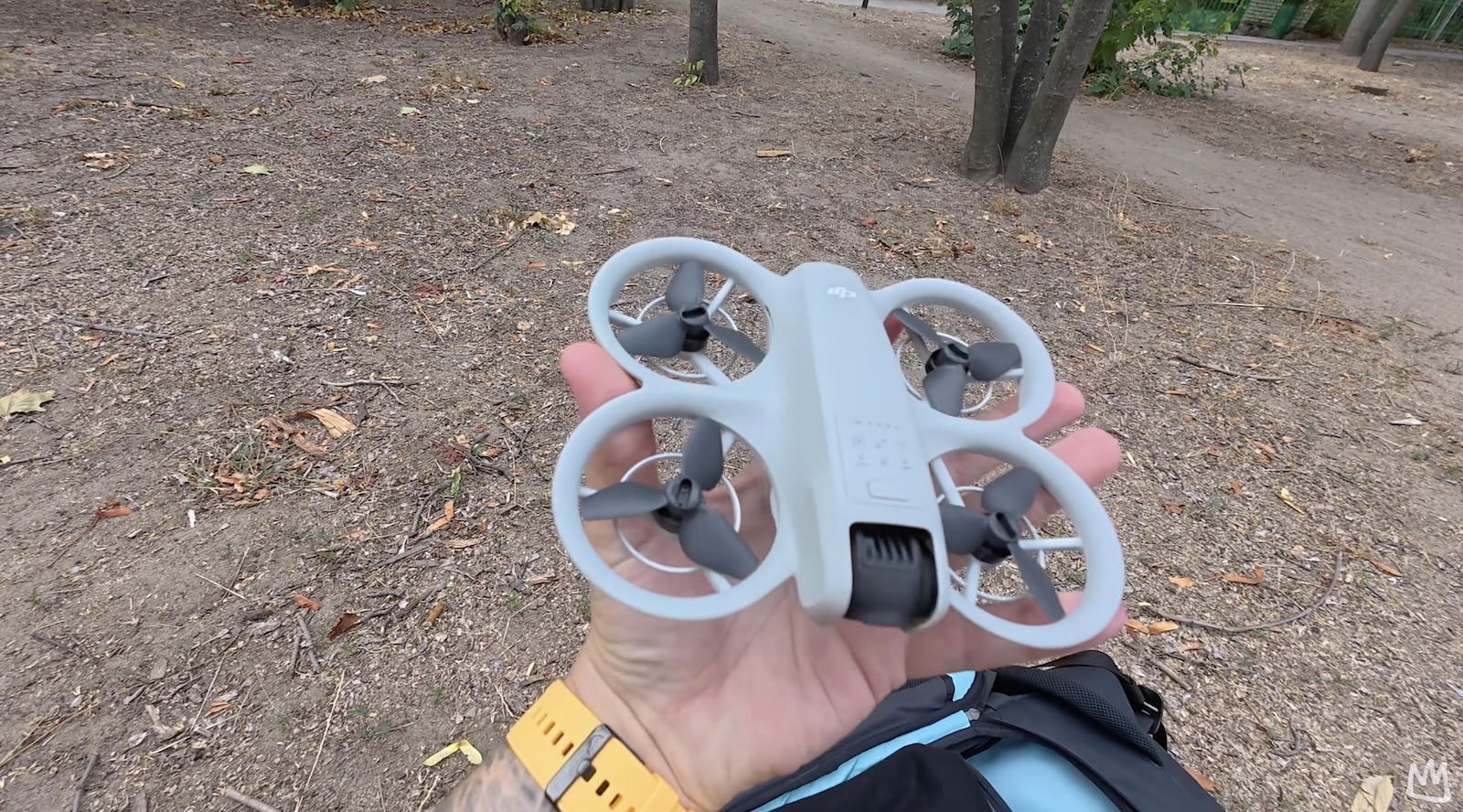 Hand holds a white ducted cinewhoop drone on a dirt forest trail.