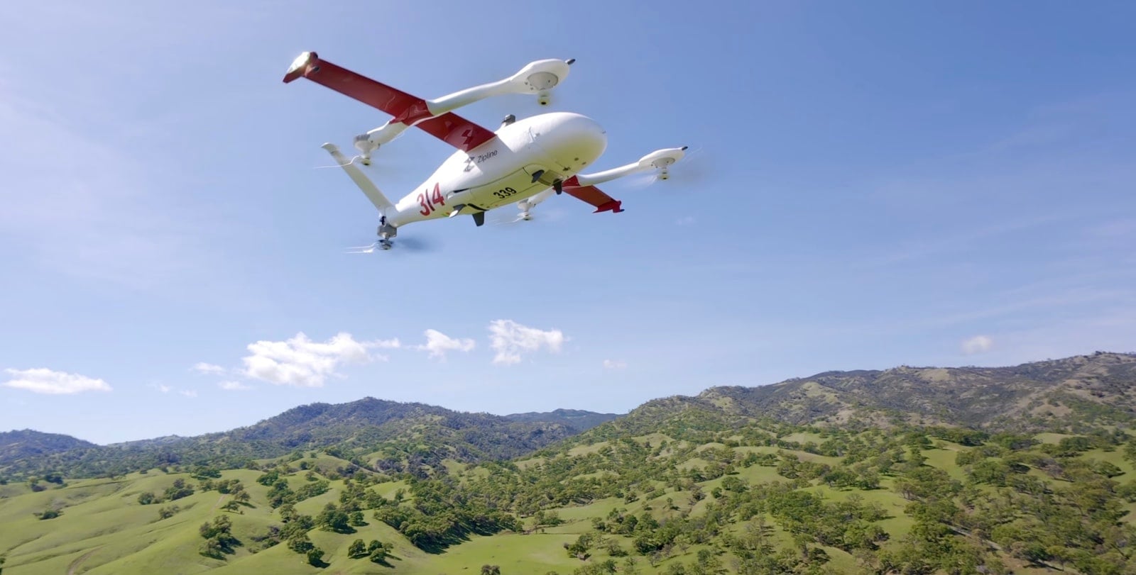 Delivery aircraft banks through blue sky above rolling green California hills.