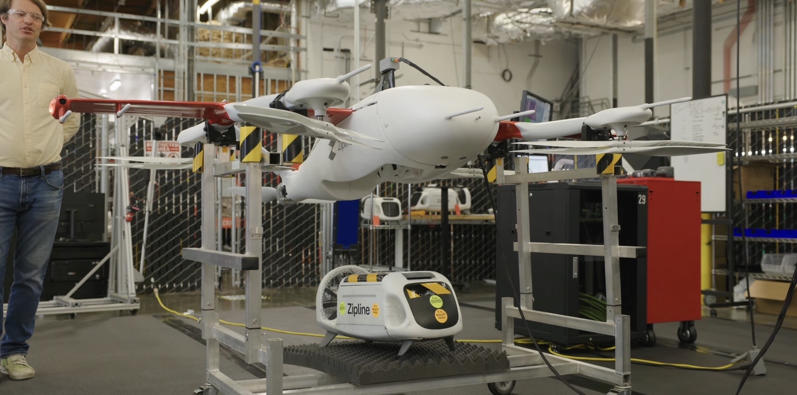 Engineer stands beside a fixed-wing Zipline aircraft loaded on an indoor rail.