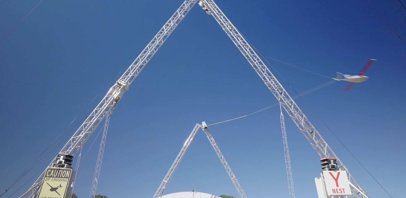 Fixed-wing aircraft approaches the catch wire strung between two tall towers.
