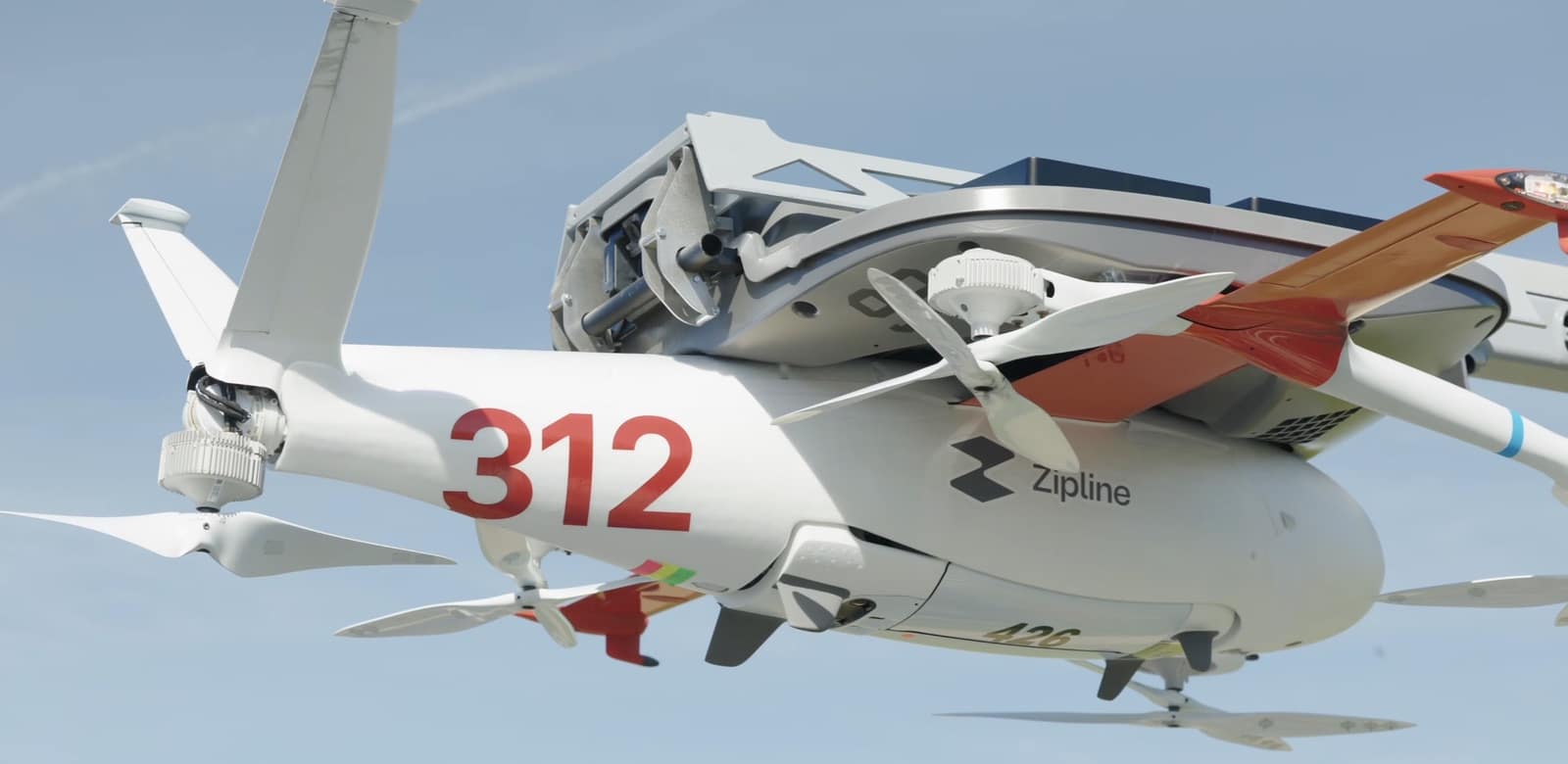 Zipline aircraft numbered 312 climbs away with its lift rotors spinning.