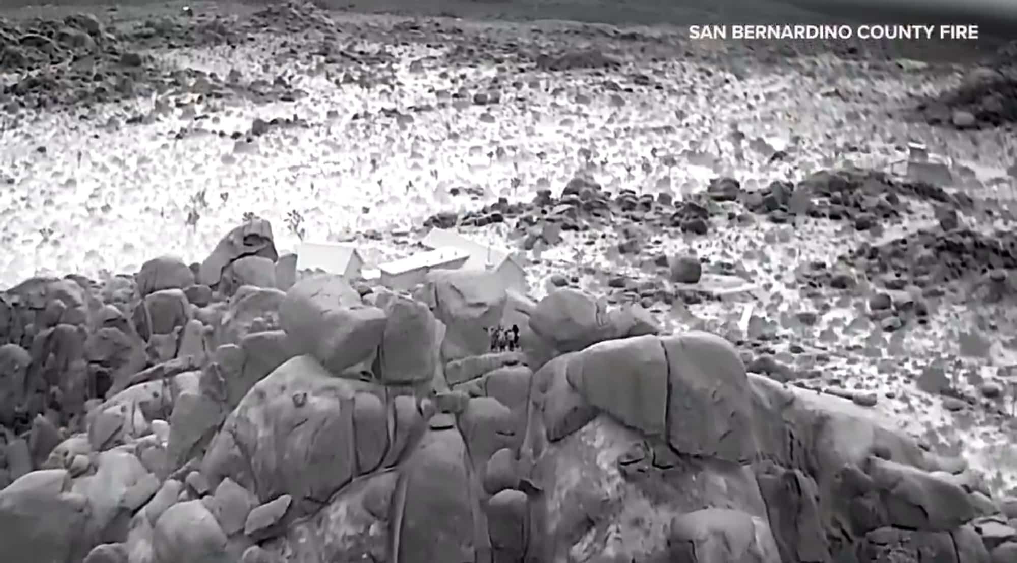 Thermal drone view of a boulder field with tiny warm figures among the rocks.