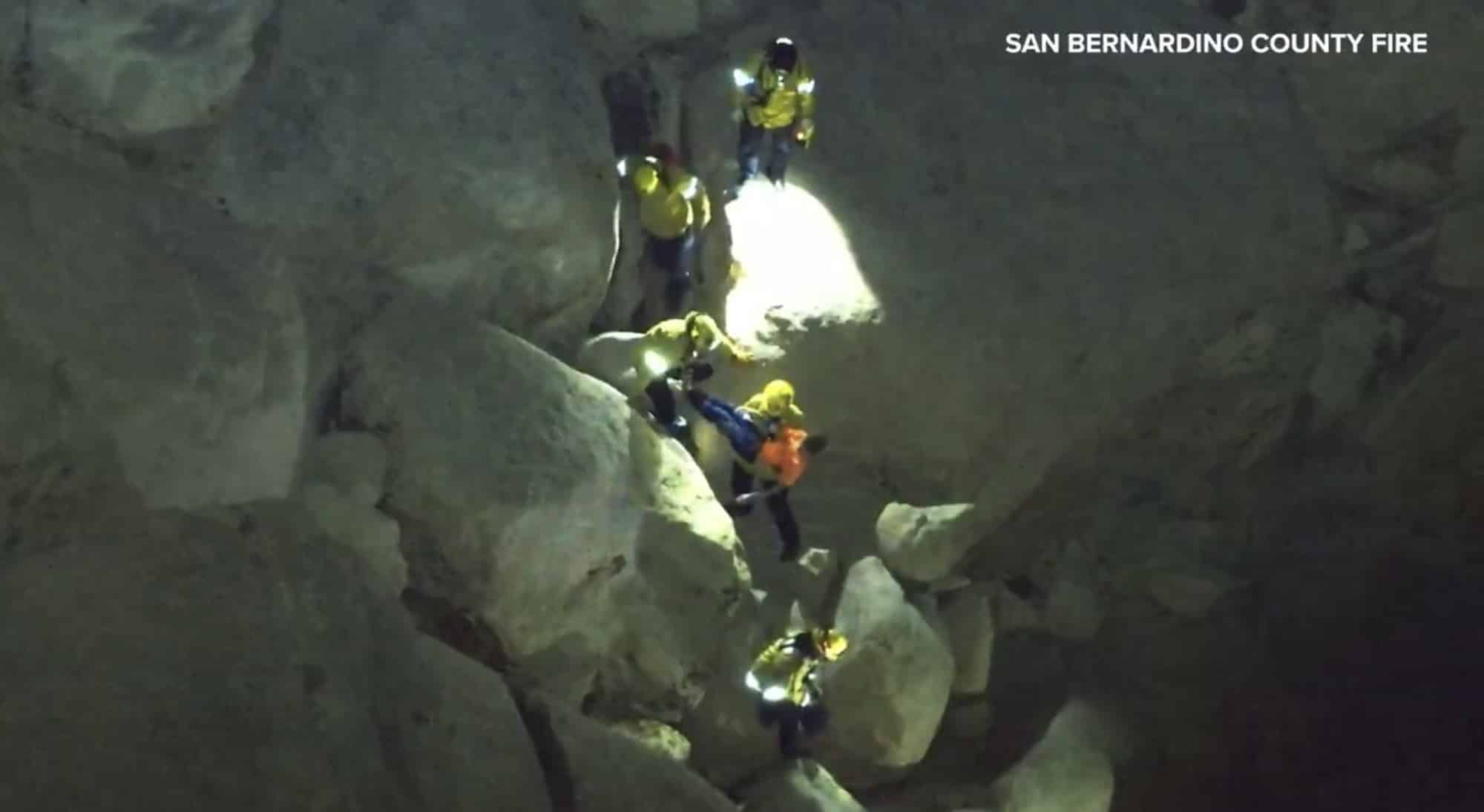 Night aerial of rescuers with headlamps spread across a jumble of pale boulders.