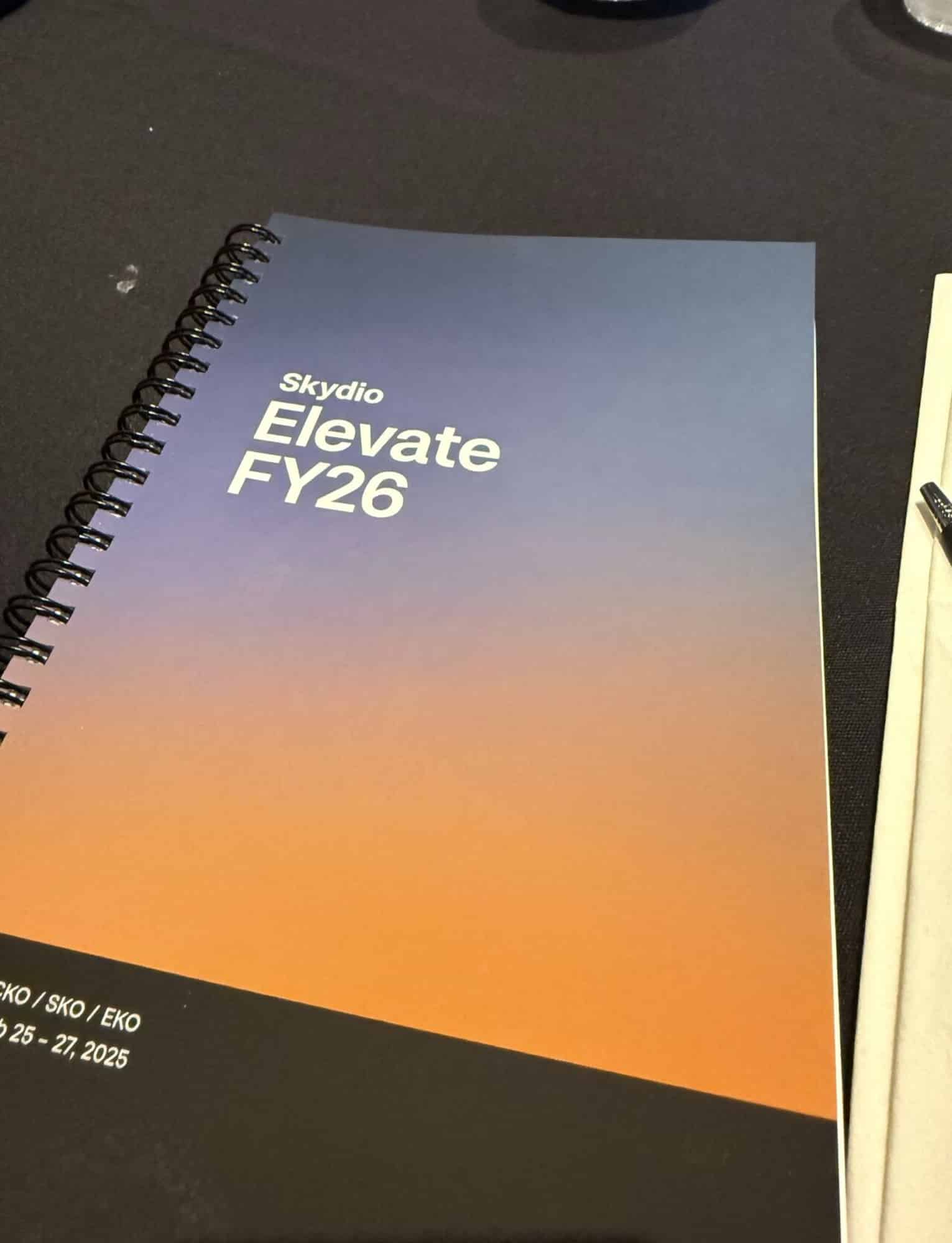 Spiral-bound Skydio Elevate FY26 conference notebook lying on a dark table.