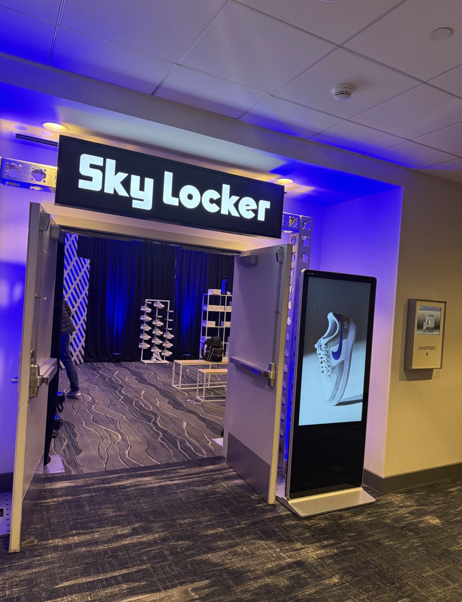 Doorway sign reading Sky Locker above shelves of sneakers under blue light.