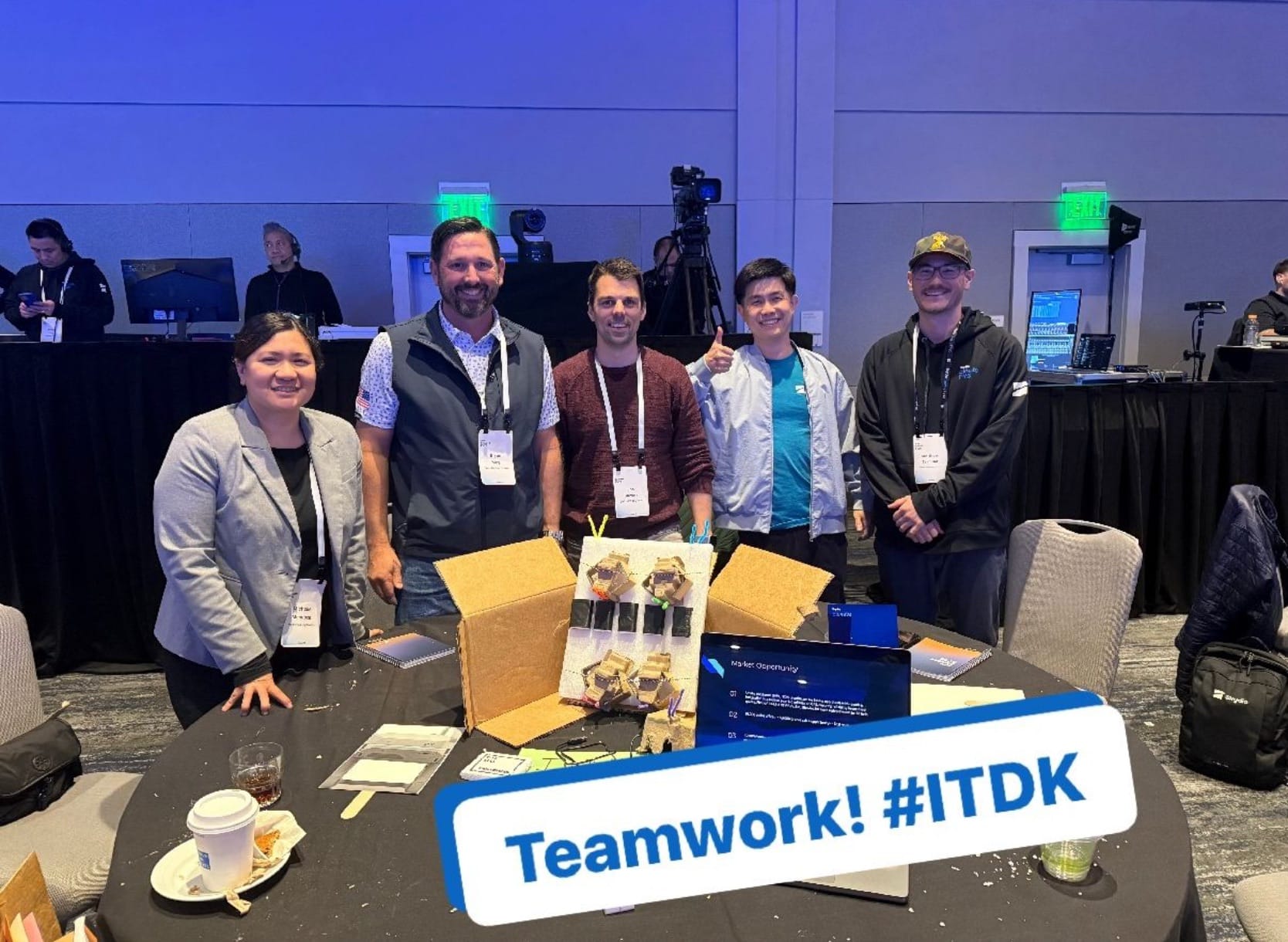 Team posed behind a table of gift boxes, captioned Teamwork.