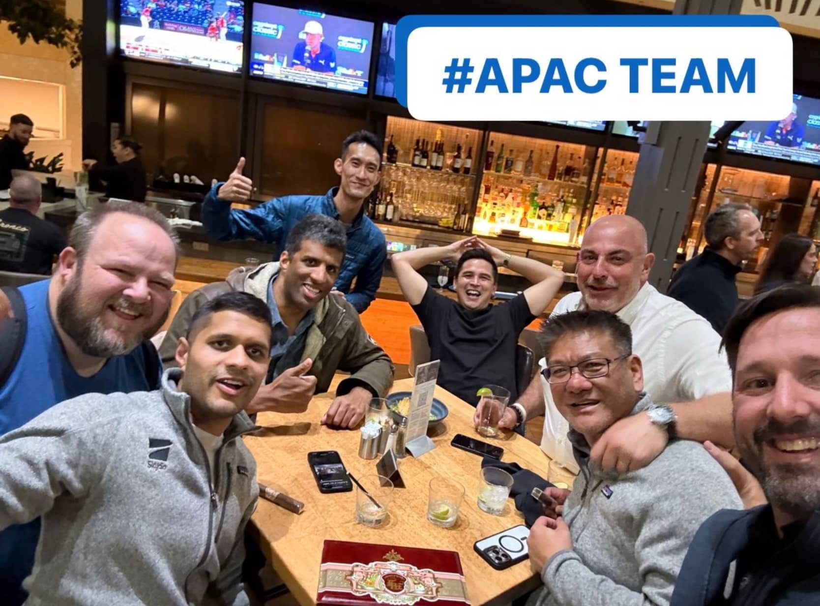 Colleagues crowded around a bar table under a caption reading APAC TEAM.