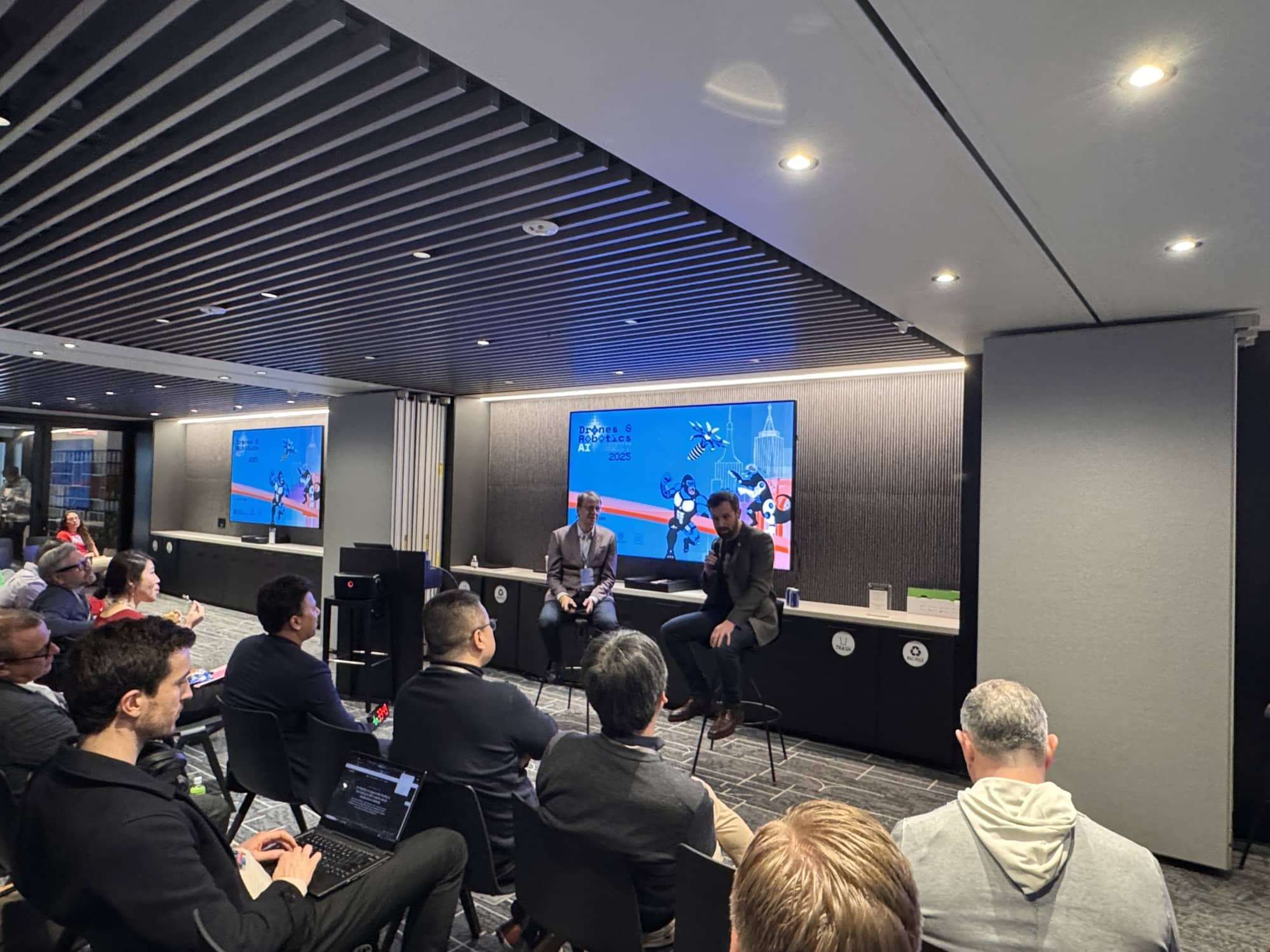 Two panelists sit on stage in front of a blue conference slide.