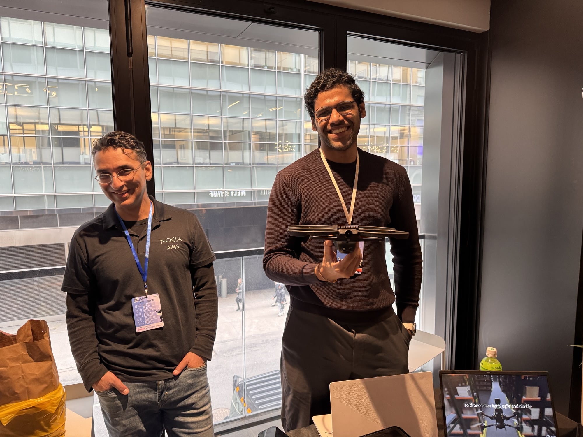 Two exhibitors by a window, one holding a small black quadcopter.