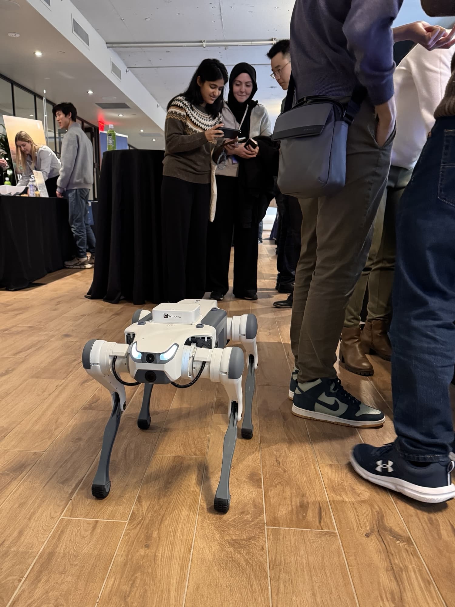 A white four-legged robot walks the floor among attendees during a break.
