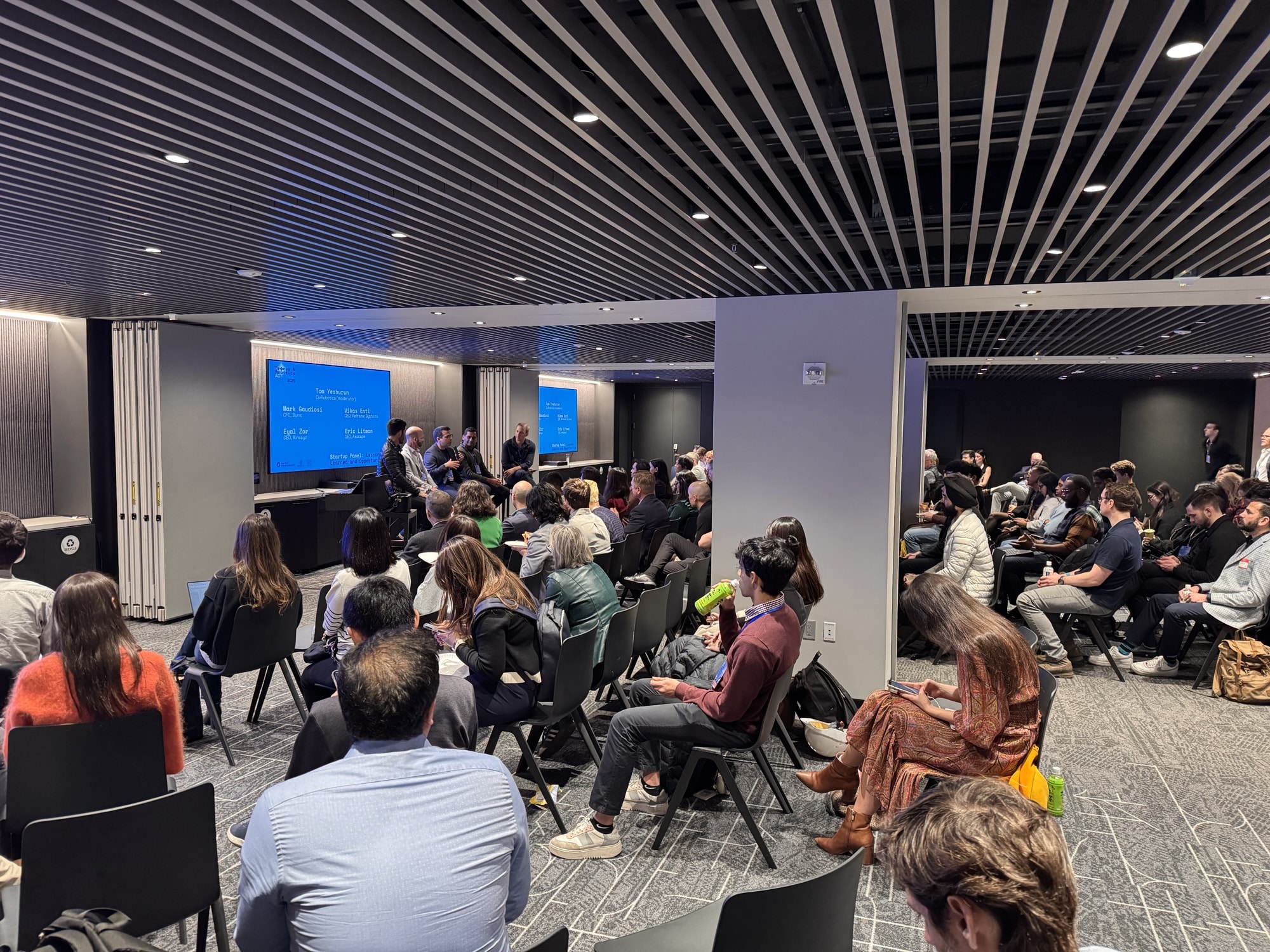 Attendees fill rows of chairs facing the stage screens in the summit room.