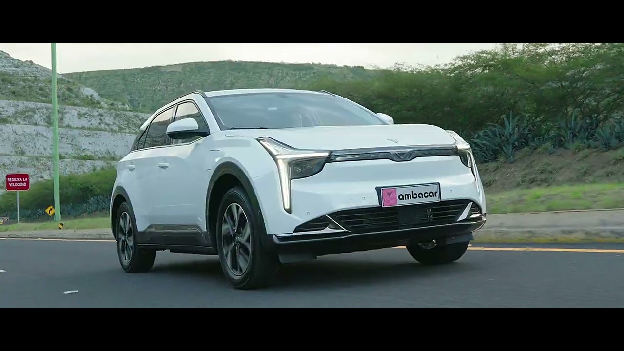 A white electric crossover drives along a hillside road in a dealer commercial.