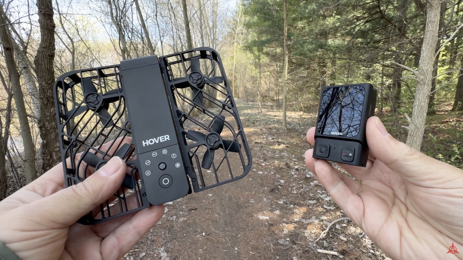 Hands holding a folded HoverAir X1 and its Beacon controller in a bare forest.