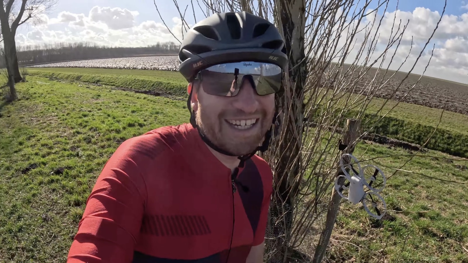 A grinning cyclist stands beside the hedgerow where the drone came to rest.