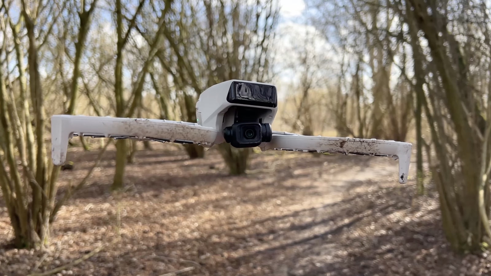 The mud-splattered DJI Flip hovers low along a path through coppiced woodland.