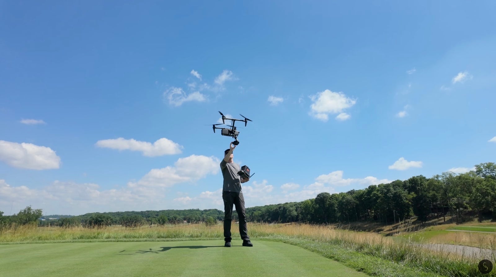 A pilot lifts the large cinema drone overhead on a mown golf fairway.
