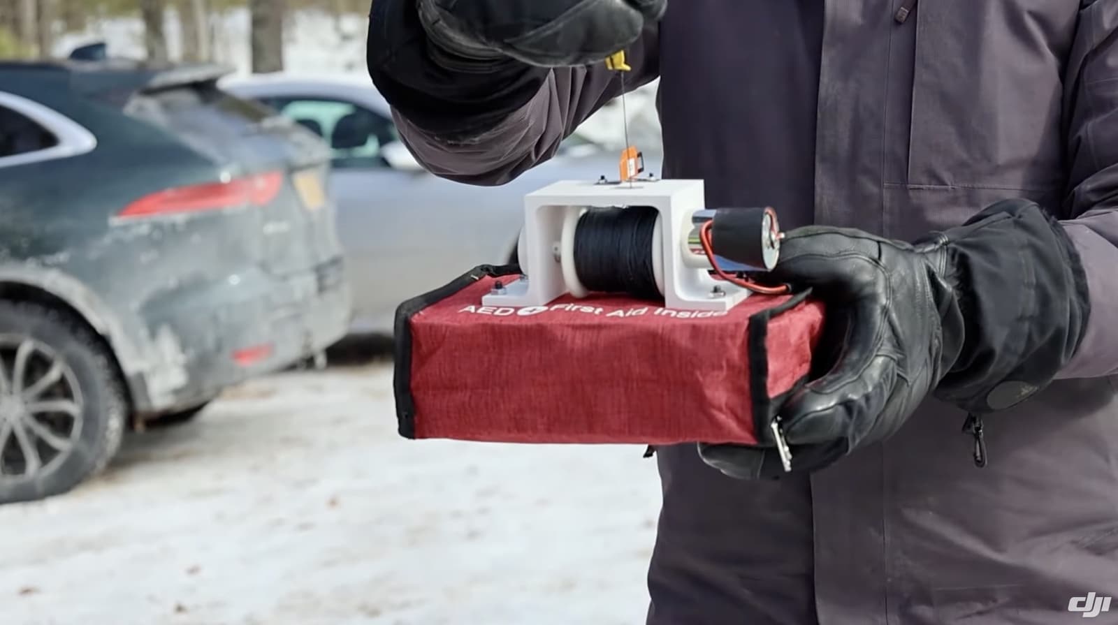 Gloved hands hold a red defibrillator case rigged for aerial release.