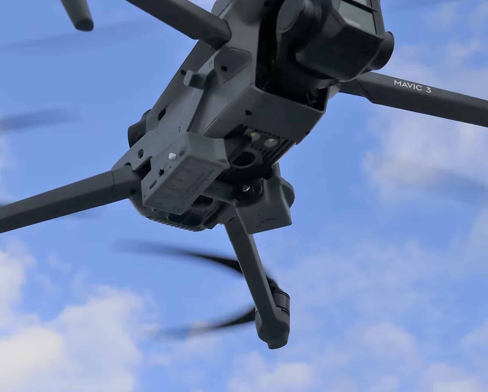Underside of a DJI Mavic 3 in flight against a bright blue sky.