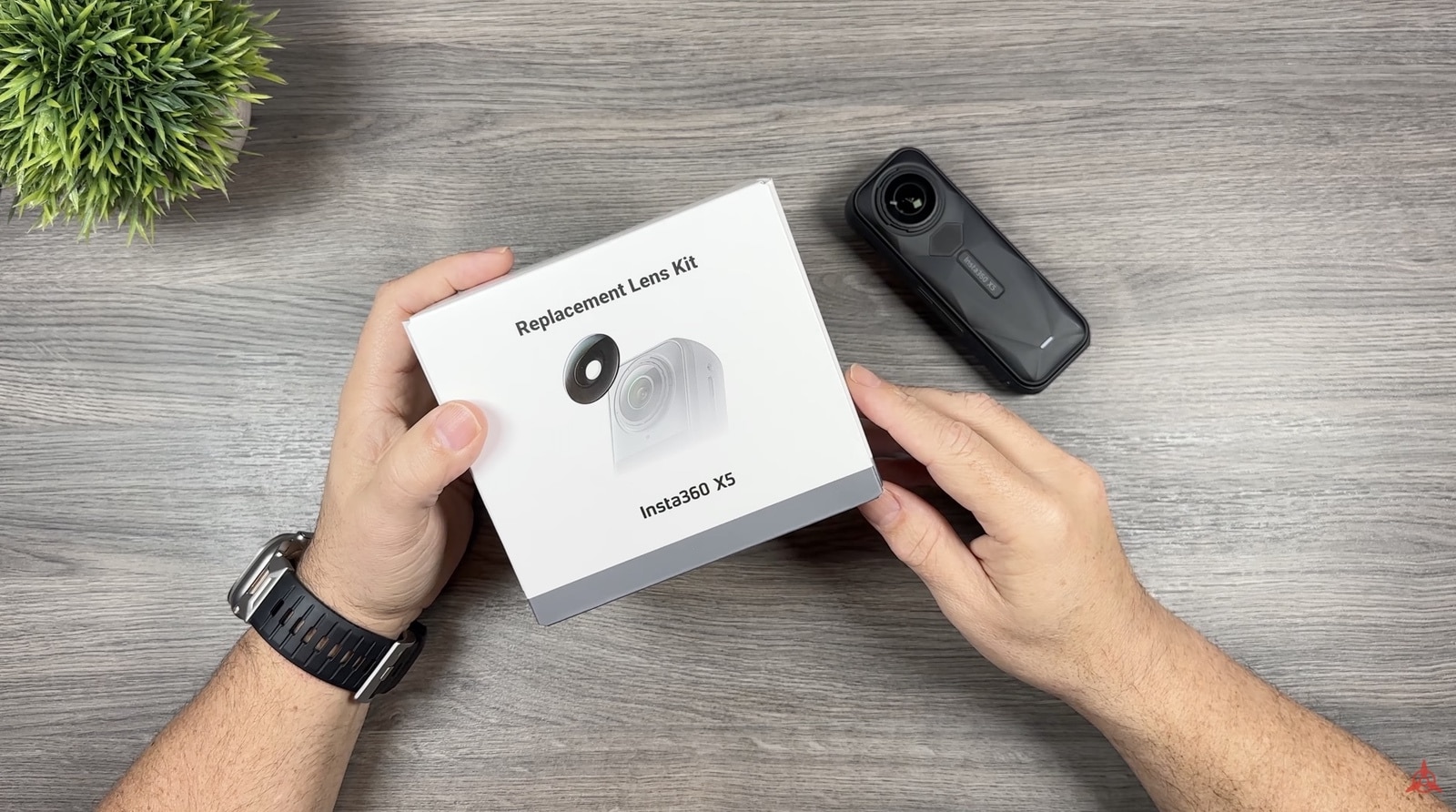 Hands holding the Insta360 X5 replacement lens kit box beside the camera.