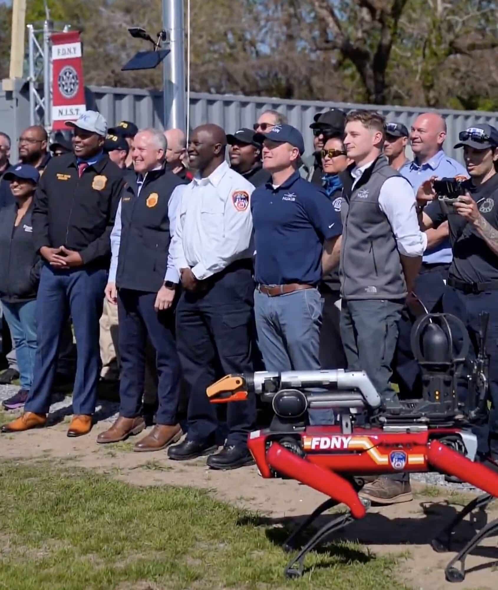 Firefighters and officials lined up behind a red FDNY quadruped robot outdoors.