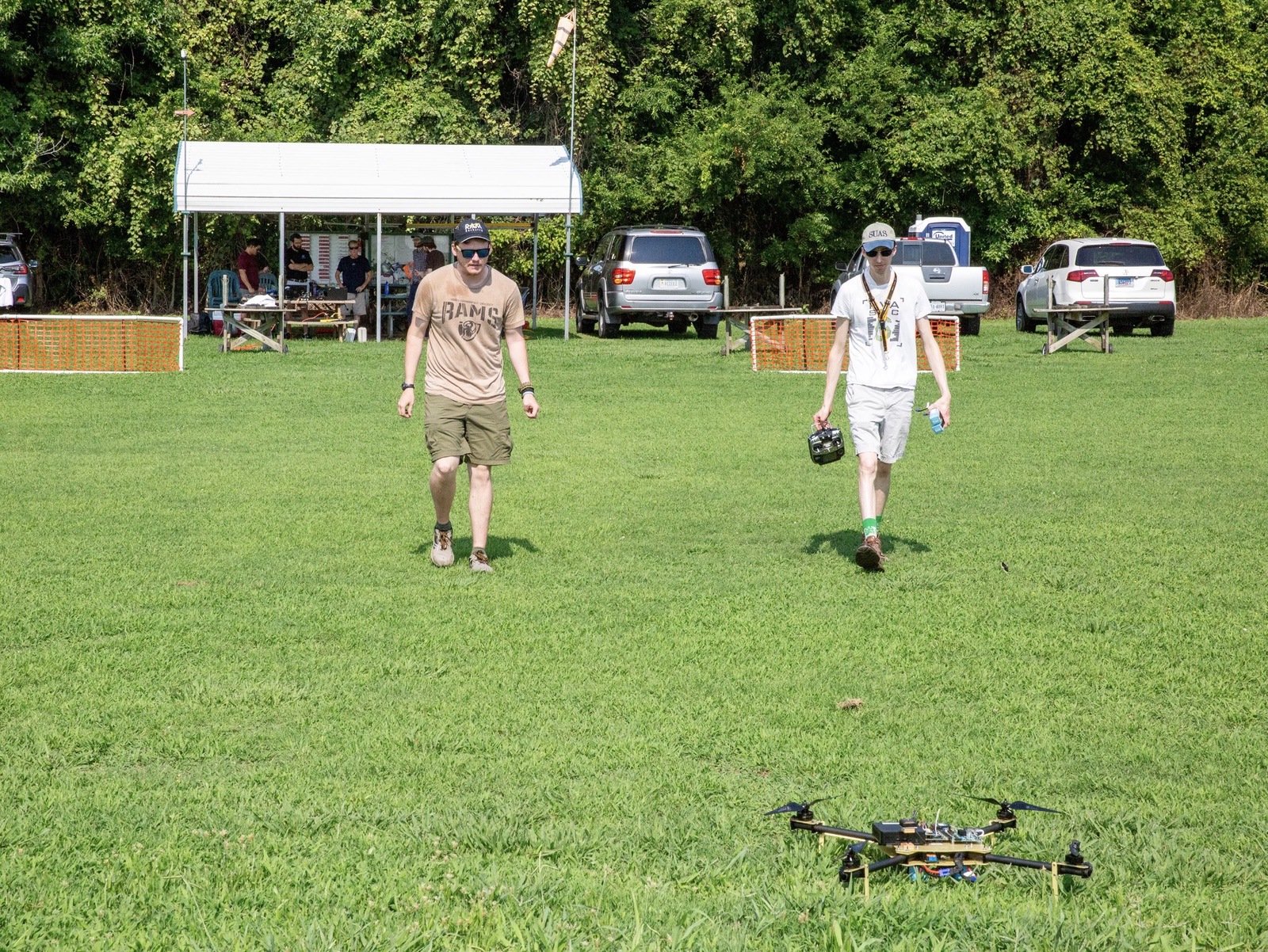 Crew members walk across a grass test field toward a small multirotor drone.