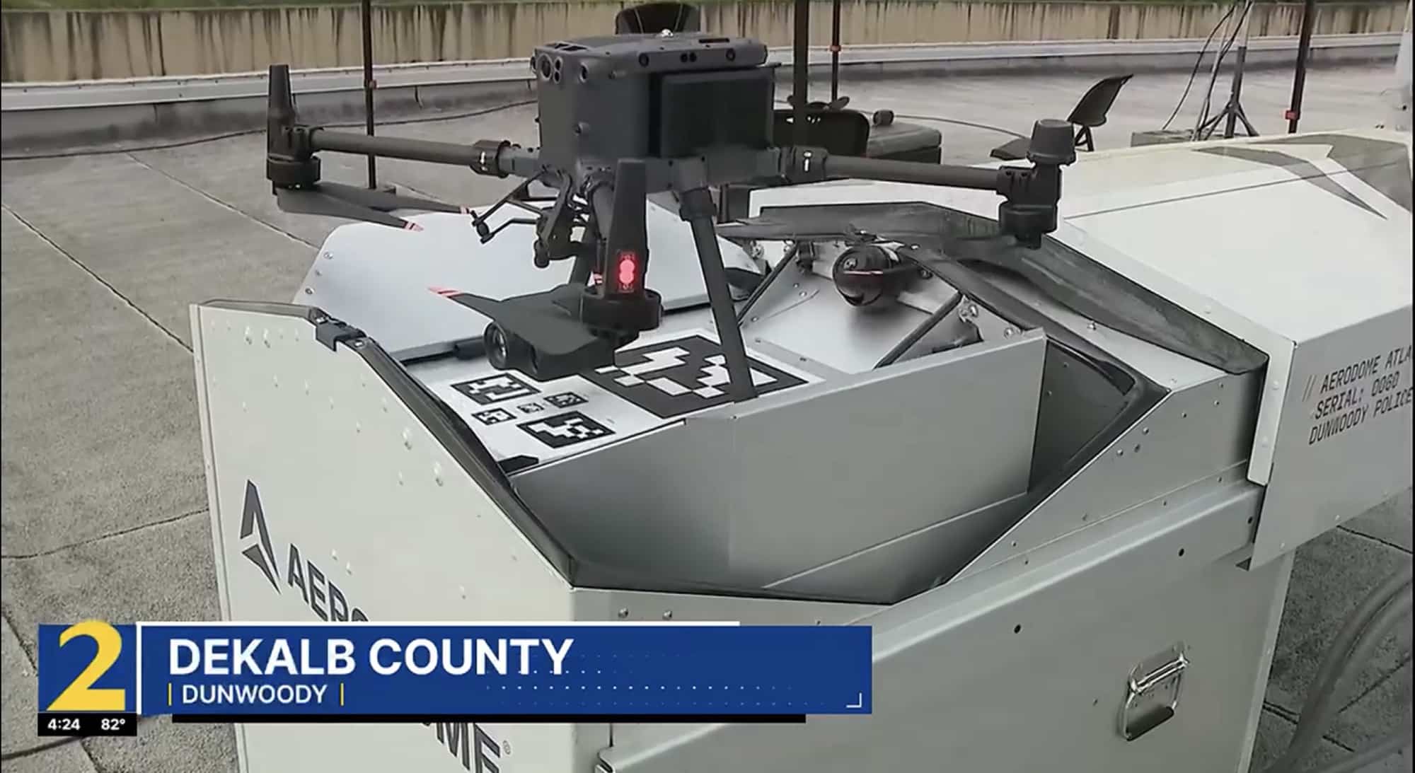 A drone sits on an open rooftop nest under a news chyron naming Dunwoody.