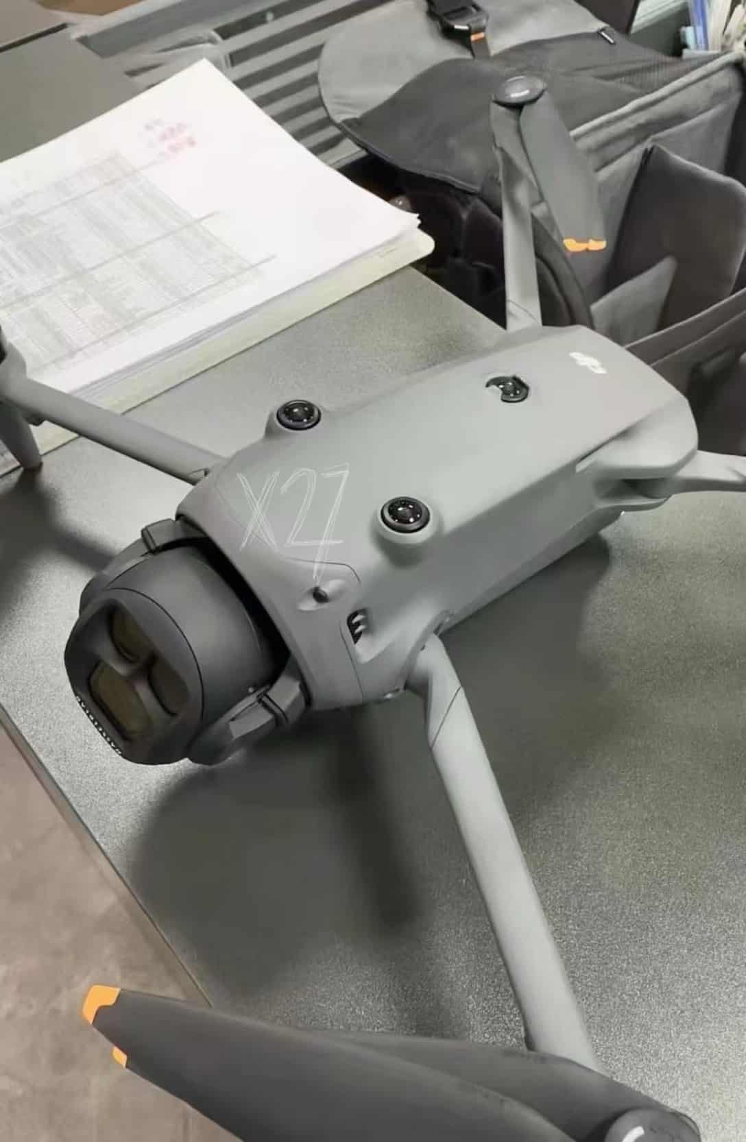 A grey prototype airframe marked X27 sits on a bench beside printed test sheets.