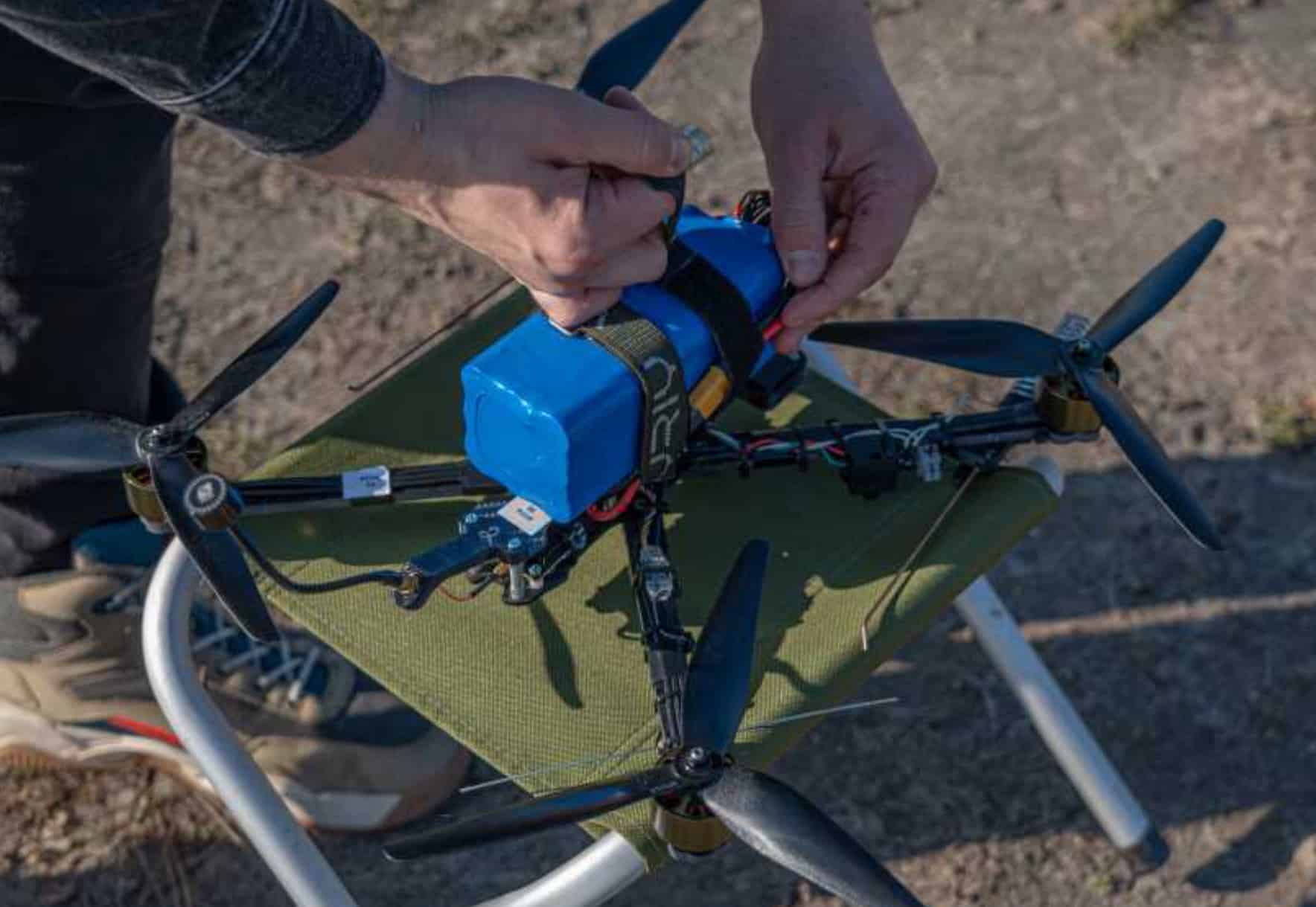 Hands fit a blue payload block onto a large multirotor sitting on the ground.