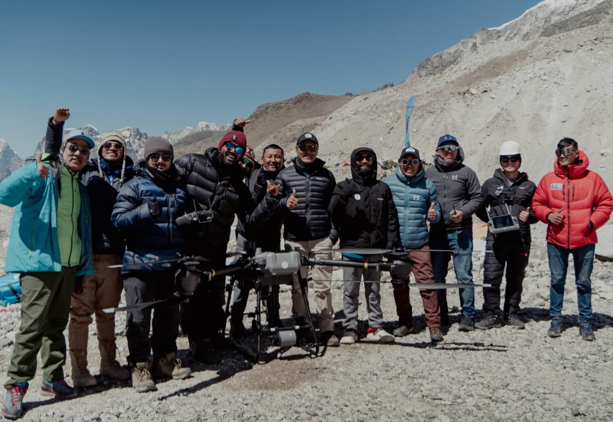 Expedition team posing with a cargo drone on the glacier moraine at base camp.