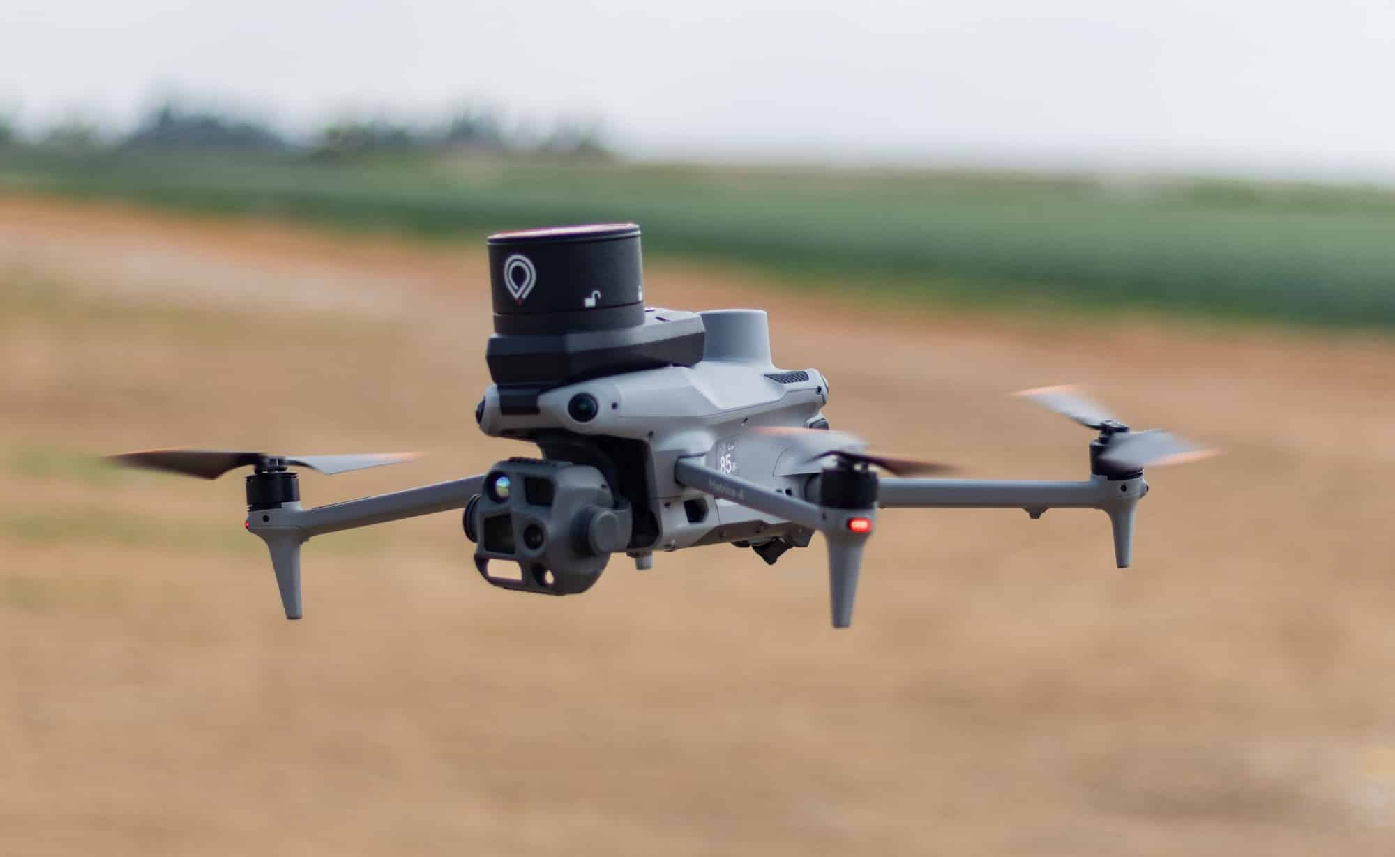 Drone carrying the ParaZero recovery unit hovers low above a farm field.