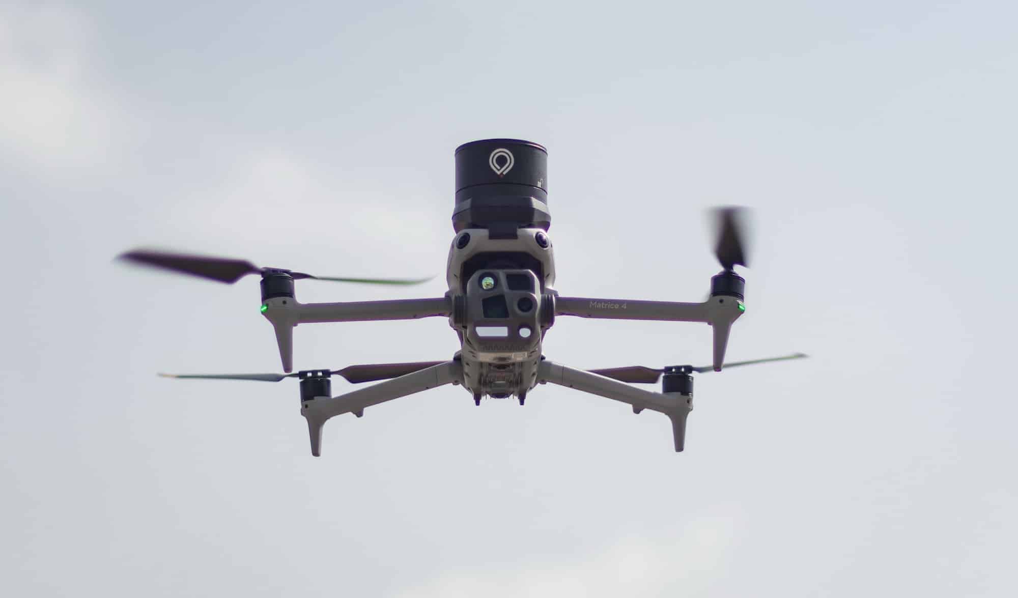 Matrice 4 flies overhead with a cylindrical parachute canister mounted on top.