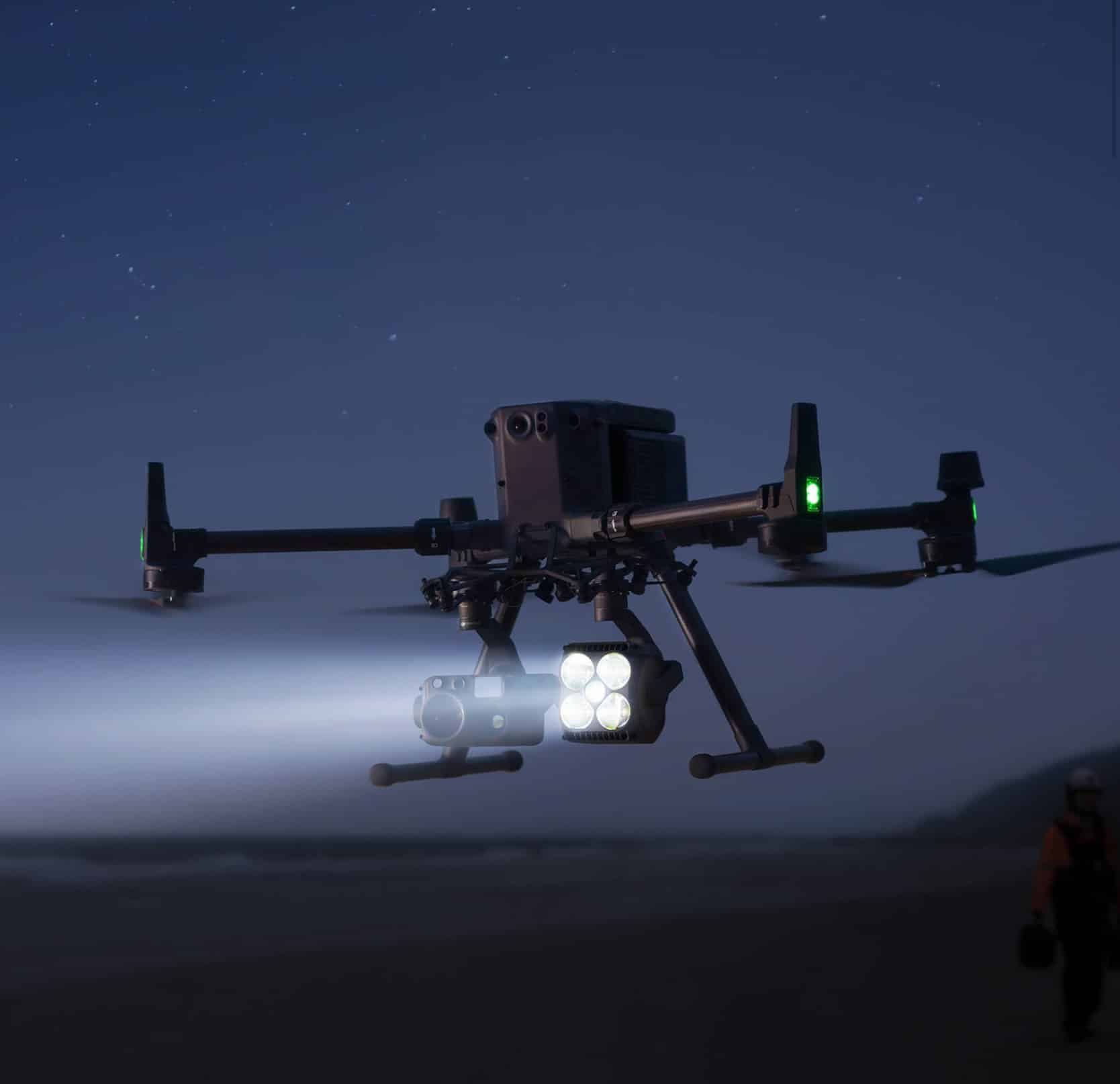 Matrice drone casting a bright spotlight beam through darkness at low altitude.