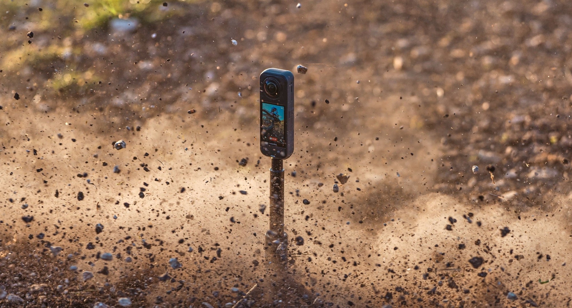 The camera on a pole is pelted by flying dirt and gravel.