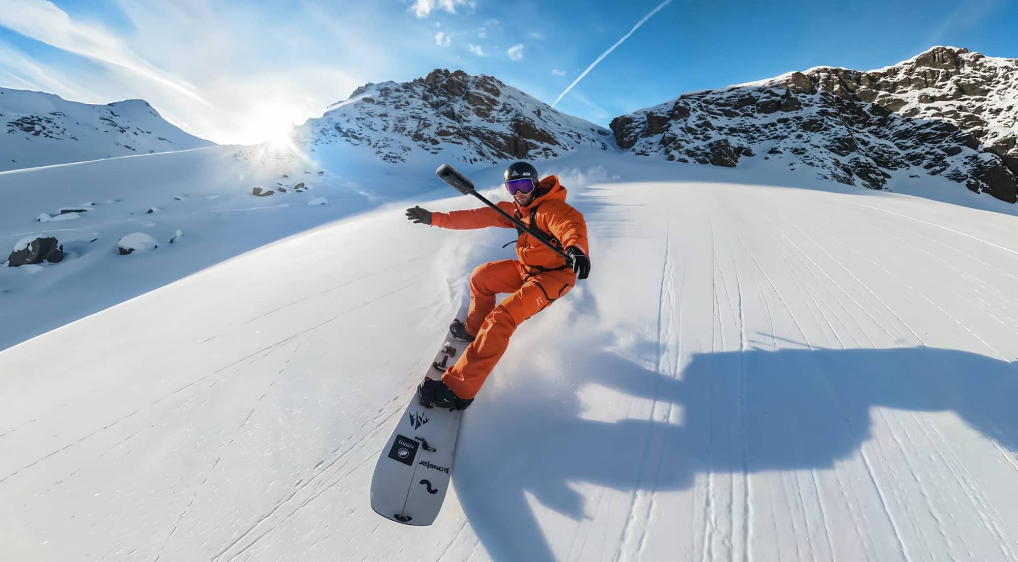 A snowboarder in orange carves a bright turn across an untracked slope.