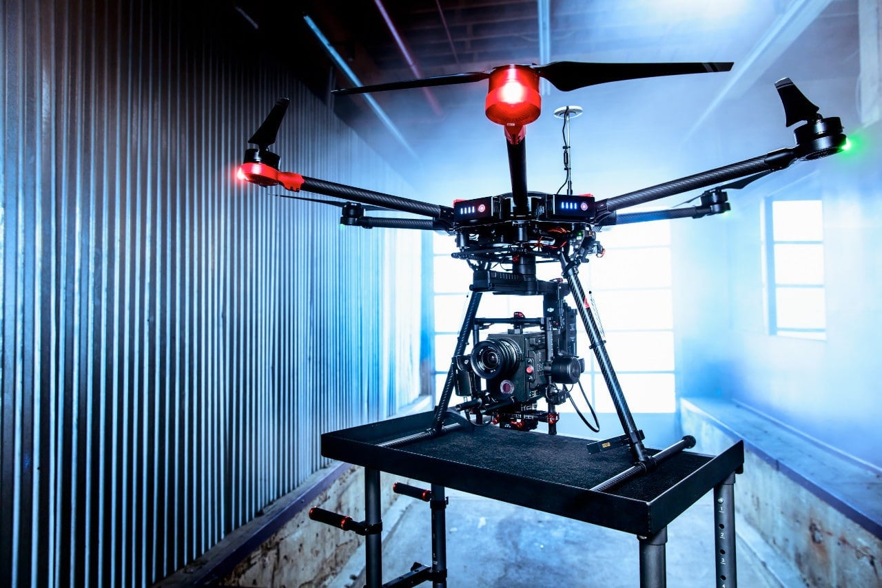 A Matrice 600 carrying a payload stands on a bench in a blue-lit hangar.