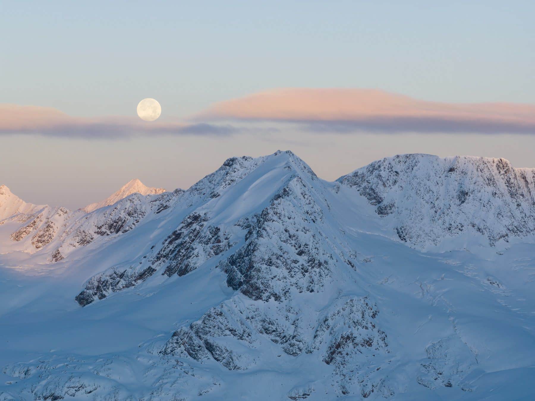 The full moon looms above a single snowy peak at 168mm equivalent.