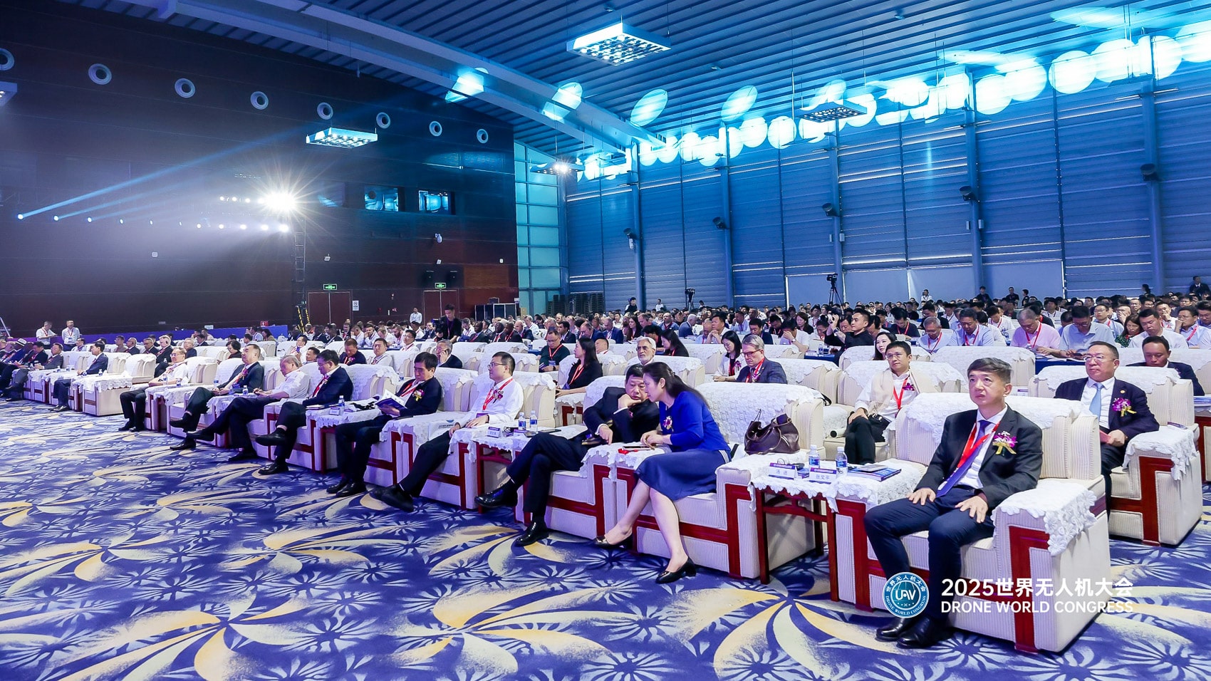 Delegates fill round tables in a blue-lit conference hall.