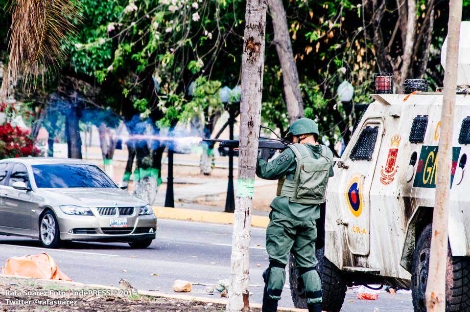 A helmeted national guardsman stands beside an armoured vehicle on a Venezuelan street.