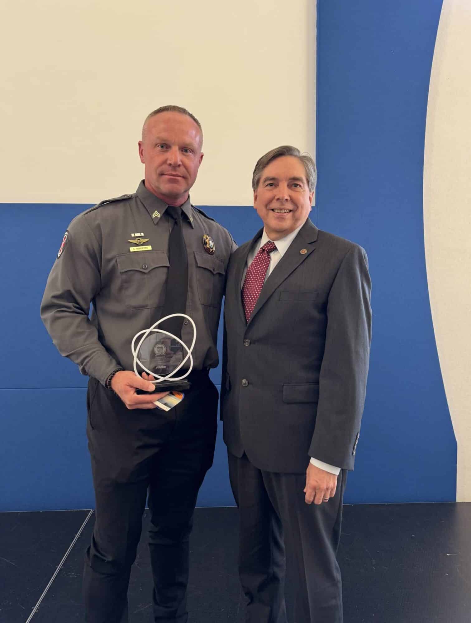 A uniformed search and rescue captain holds his trophy beside a man in a suit.