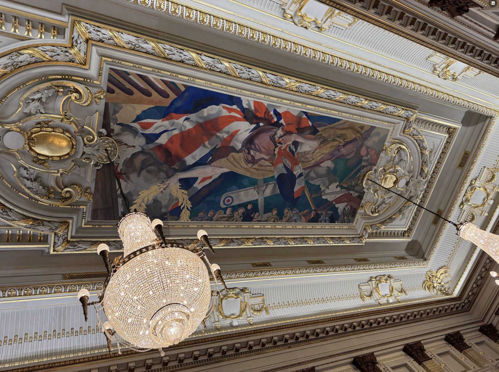 Ornate painted ceiling and chandelier of the hall, a Union Jack in the mural.