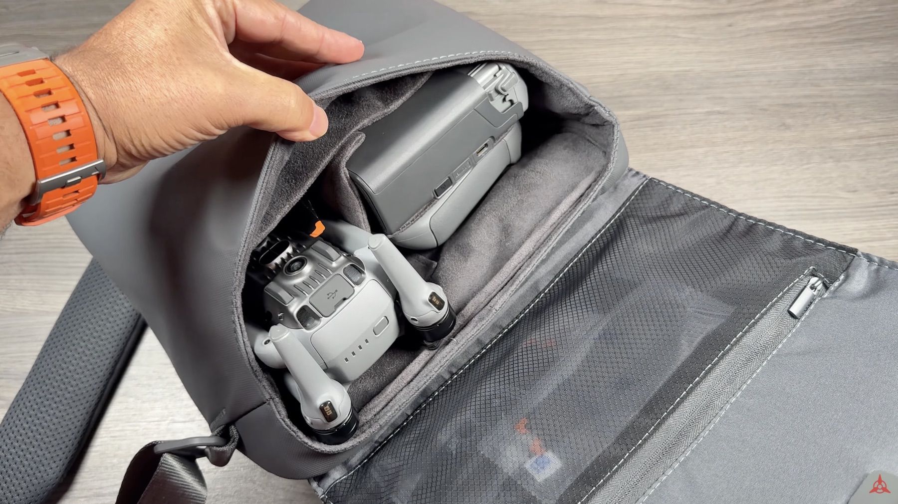 A hand slides the folded drone into the padded sleeve of a shoulder bag.