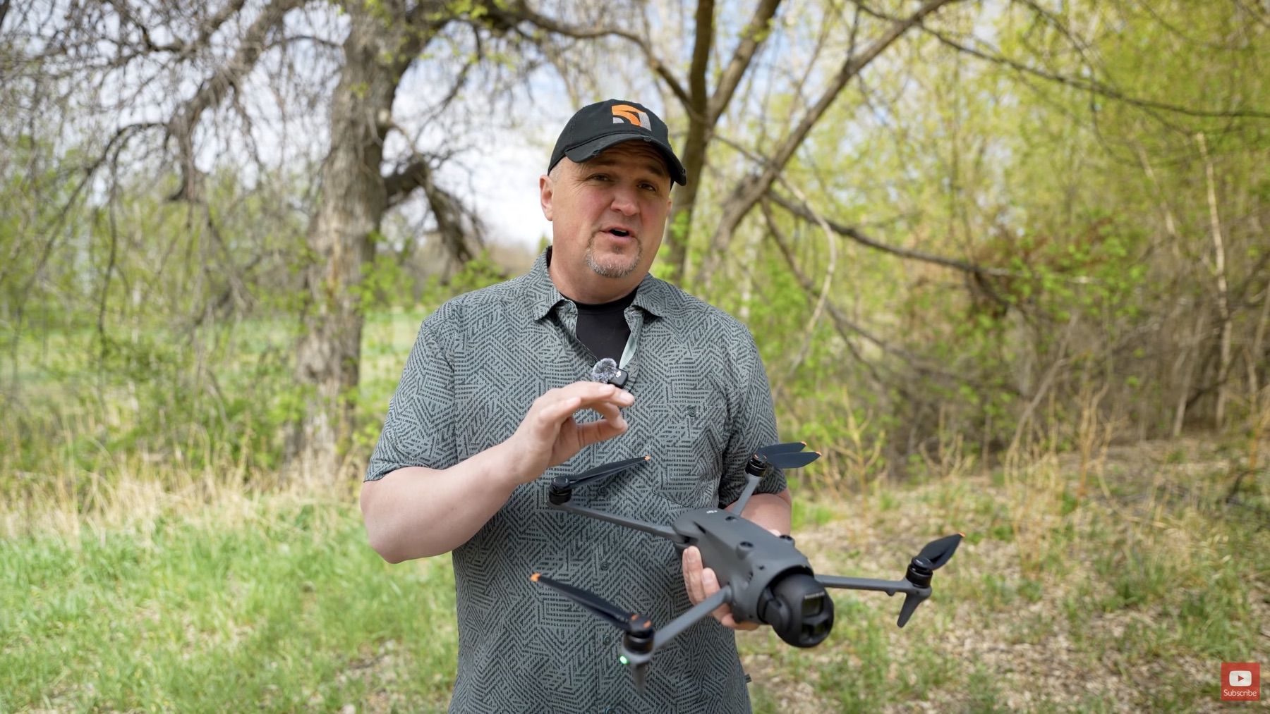 A reviewer in a cap holds the unfolded Mavic 4 Pro in front of bare trees.