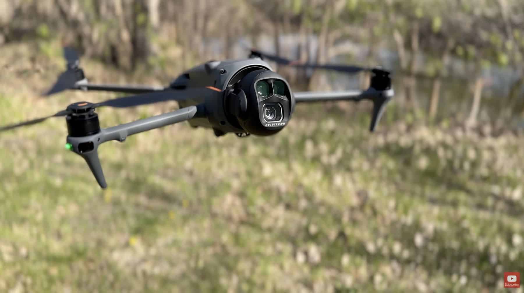 The Mavic 4 Pro hovers low over grass with its triple-camera gimbal forward.