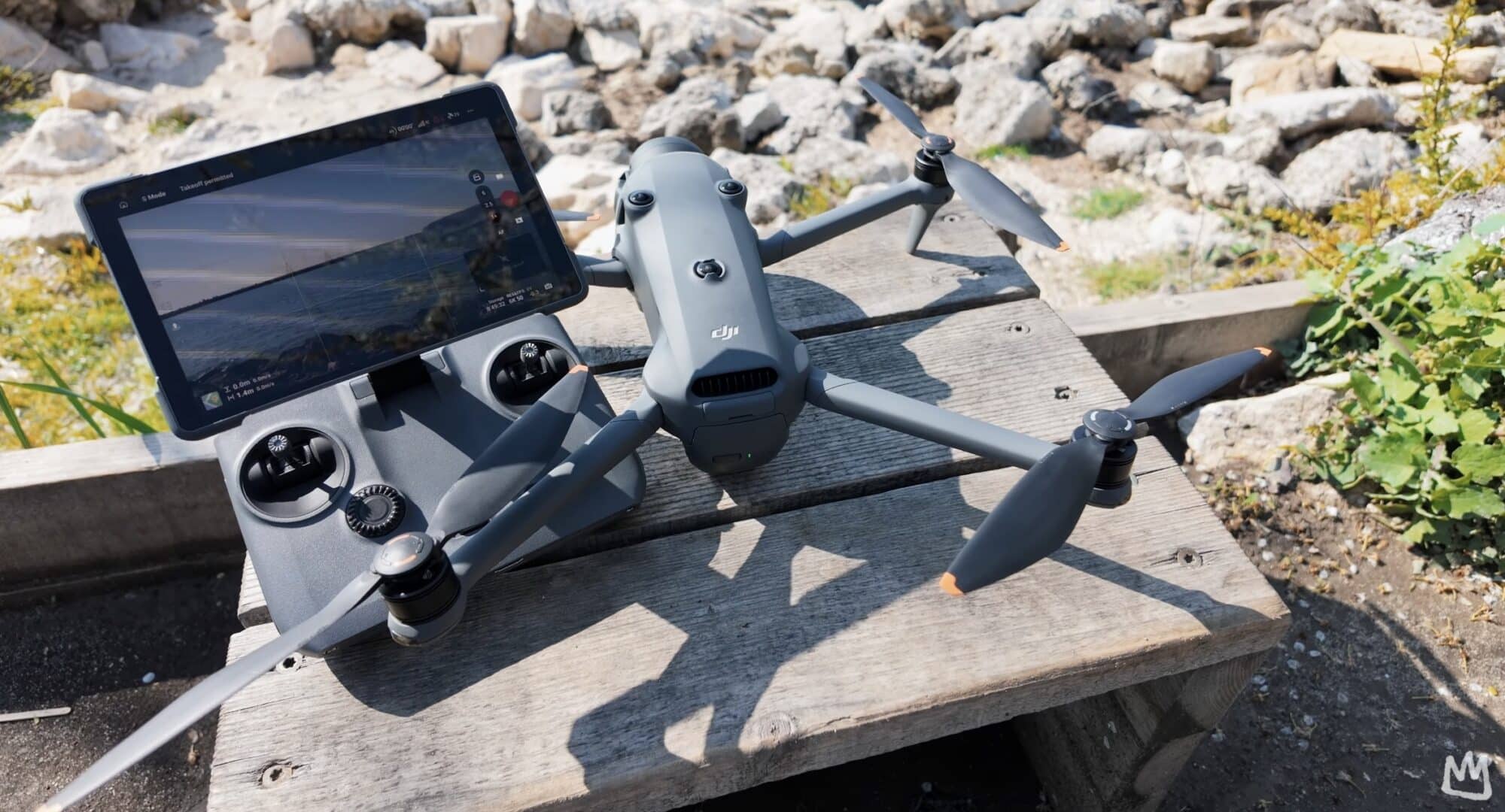 The drone and its screen controller sit unfolded on a wooden bench outdoors.