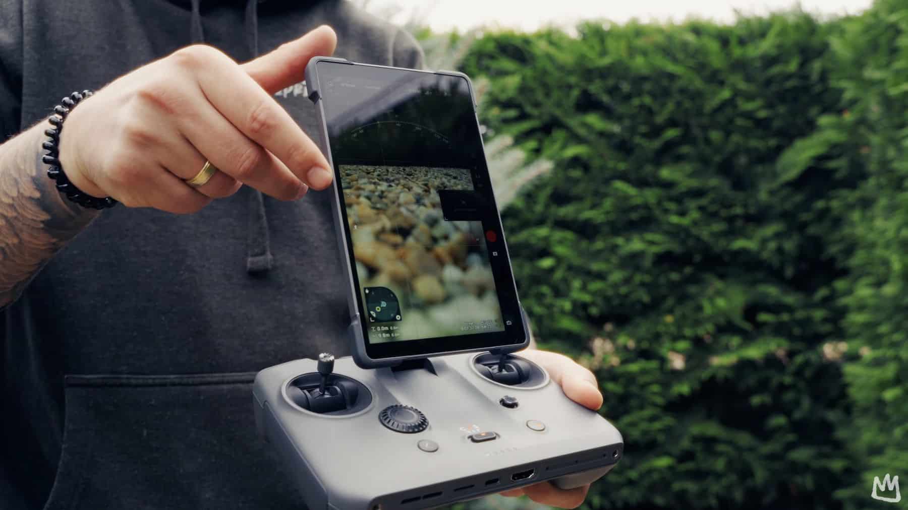Reviewer tilting the RC Pro 2 screen into portrait beside a tall hedge.