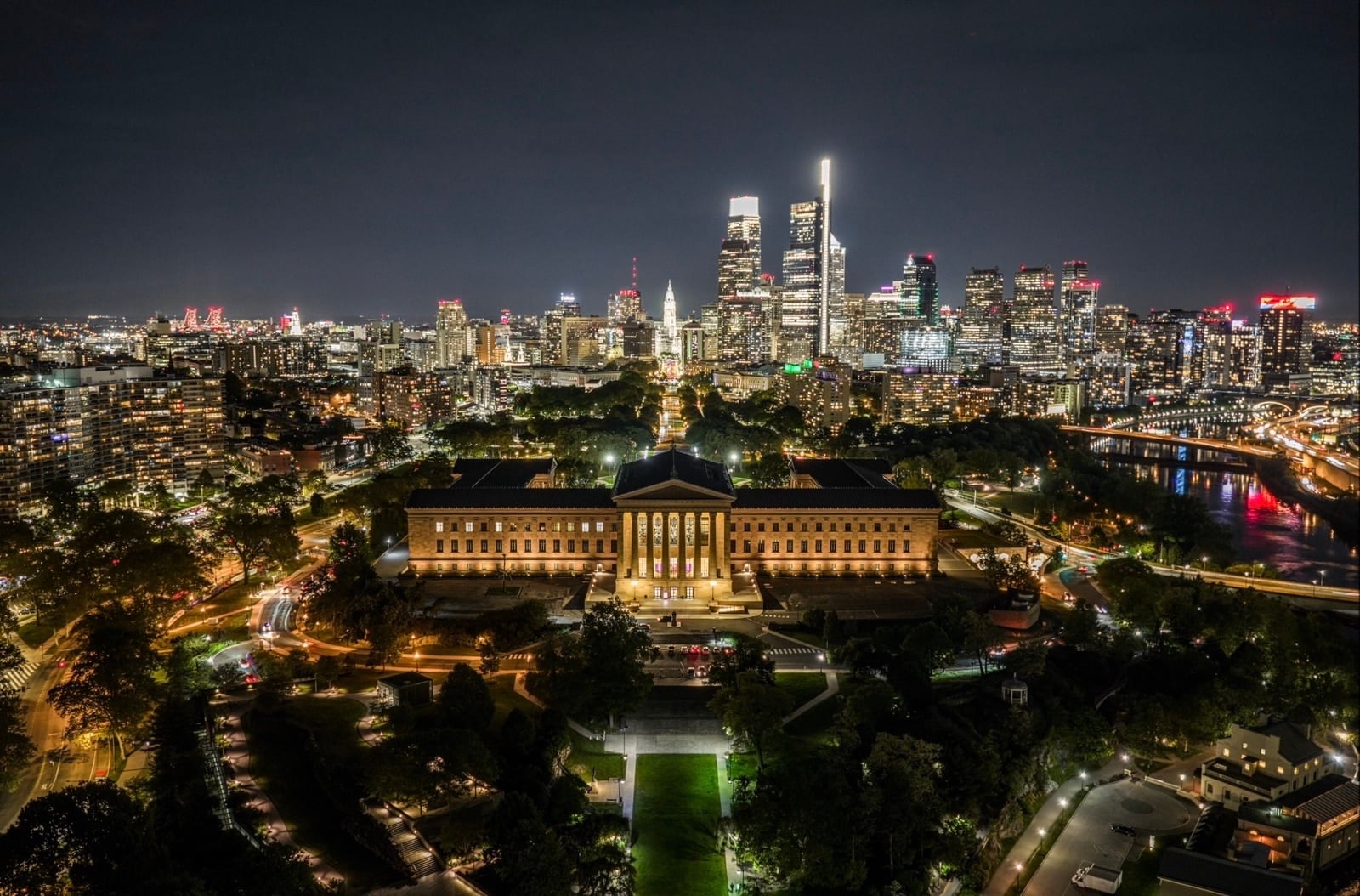 The floodlit Philadelphia Museum of Art glows below the city skyline after dark.